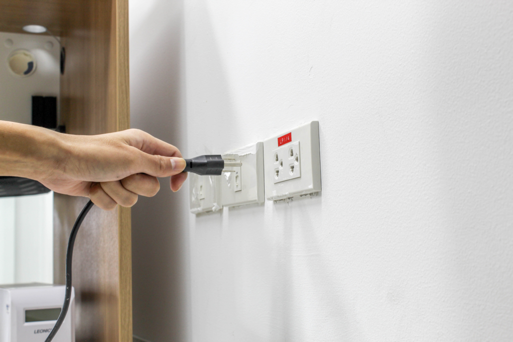 A hand holding a plug in to a wall outlet
